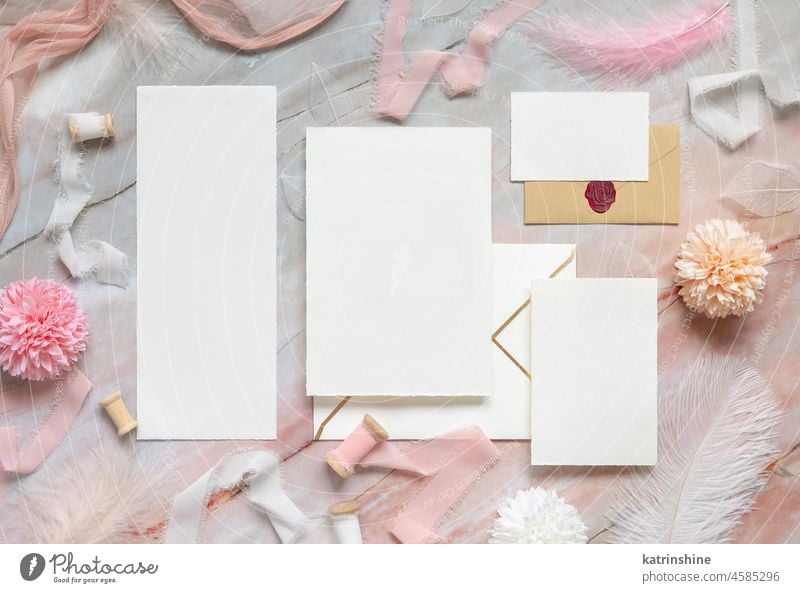 Hochzeitskarten und Umschläge zwischen pastellfarbenen Blumen, Seidenbändern und Federn auf Marmor Kuvert Bändchen Murmel Attrappe rosa Draufsicht mädchenhaft