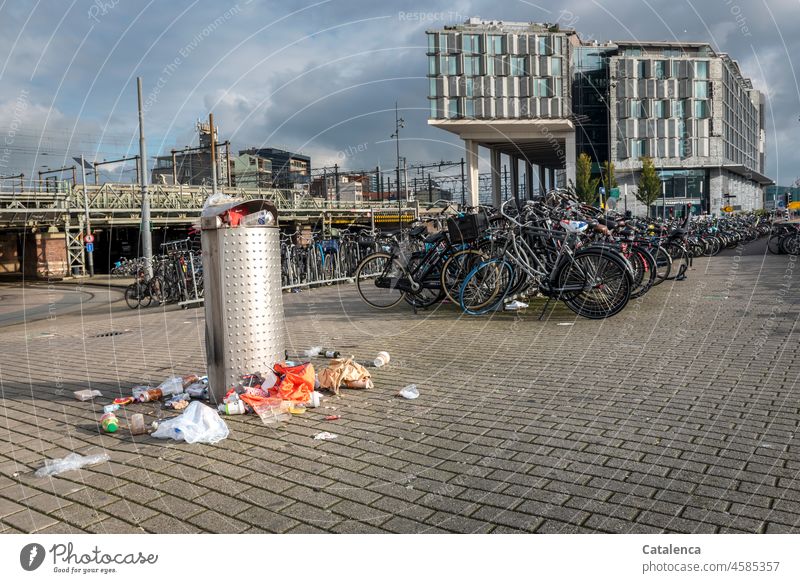 Überquellender Müllbehälter einer Stadt Voller Mülleimer verstreut Abfall Recycling entsorgen wegwerfen Umweltverschmutzung Sauberkeit Pflastesteine Fahrräder