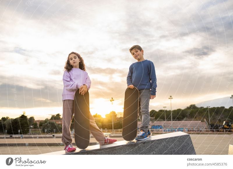 Zwei Kinder mit einem Skateboard bei Sonnenuntergang Aktion aktiv Aktivität Holzplatte Junge Paar Gesicht Frau Freunde Freundschaft Spaß Mädchen Glück Freizeit
