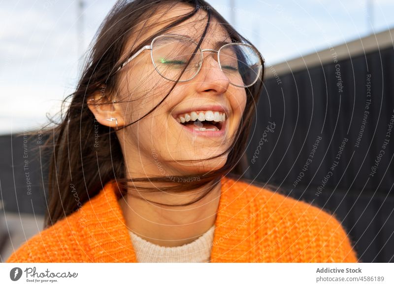 Junge, fröhliche Frau mit Brille, die sich mit geschlossenen Augen entspannt verträumt Wind gewelltes Haar positiv lässig Inhalt Strickjacke Windstille Glück