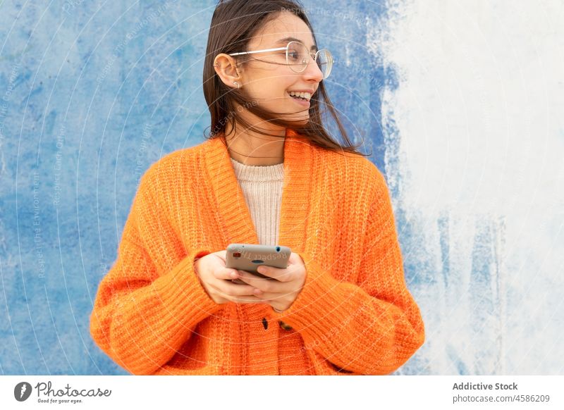 Lächelnde junge Frau mit Brille, die auf einem Handy Nachrichten schreibt Smartphone blättern Glück Beton trendy angenehm Apparatur benutzend Browsen lebhaft
