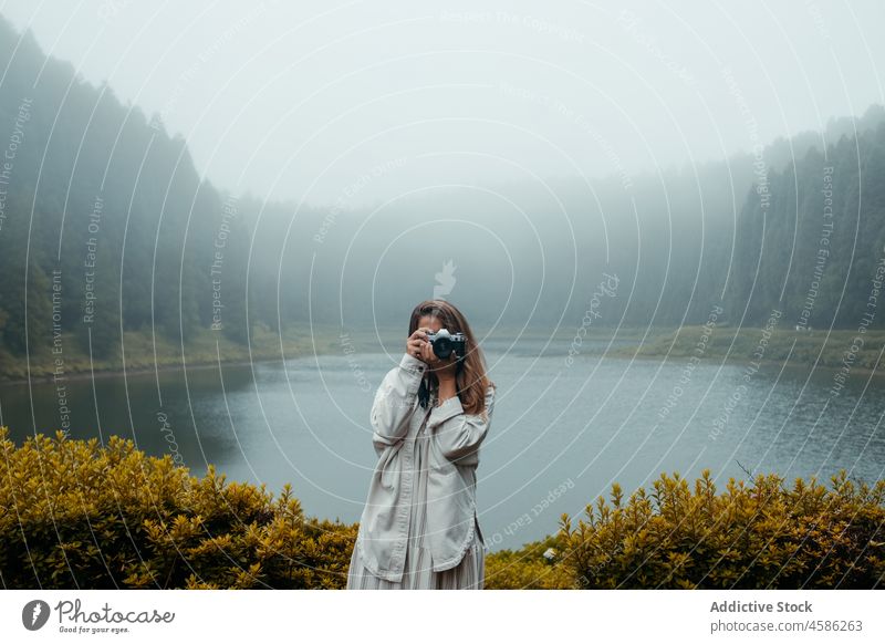 Anonyme Frau mit Kamera am See Wald Natur Nebel Fotograf Fotoapparat fotografieren reisen Urlaub Reisender benutzend Azoren São Miguel Portugal Fotografie