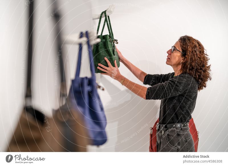 Frau hängt Handtasche an Wand in Ausstellungsraum Designer Arbeit Besitzer Sammlung Atelier Stil Kleinunternehmen Mode modern Beruf Werkstatt trendy beschäftigt
