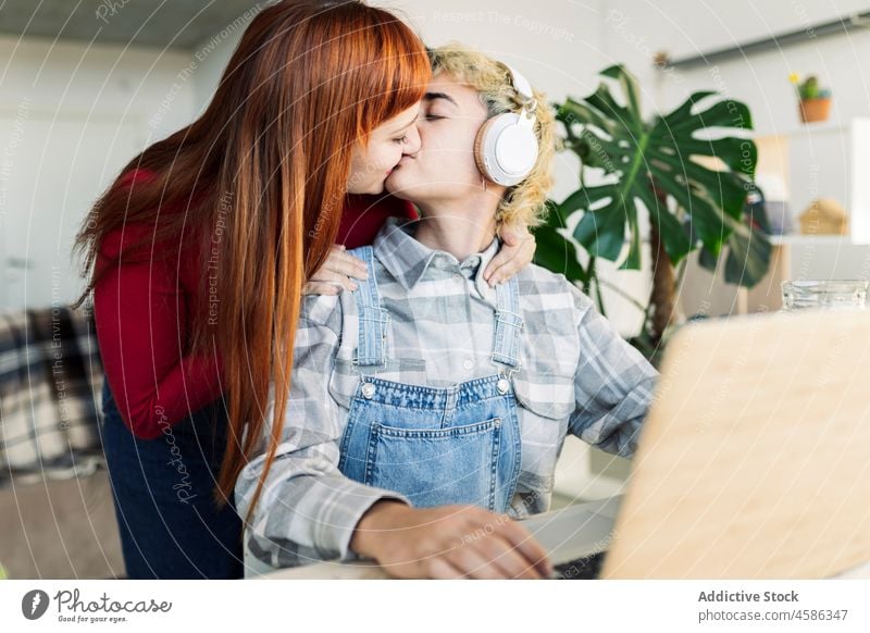 Fröhliche Lesben küssen in der Nähe von modernen Laptops Frauen Kuss Paar lesbisch Homosexualität lgbt Browsen Internet online Partnerschaft Bonden heimisch