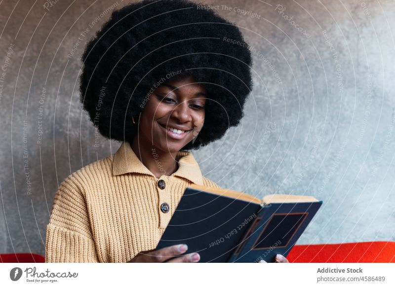 Lächelnde schwarze Frau, die auf dem Sofa ein Buch liest lesen Liege heimwärts Literatur Freizeit Komfort sich[Akk] entspannen Afroamerikaner Afro-Look achtsam