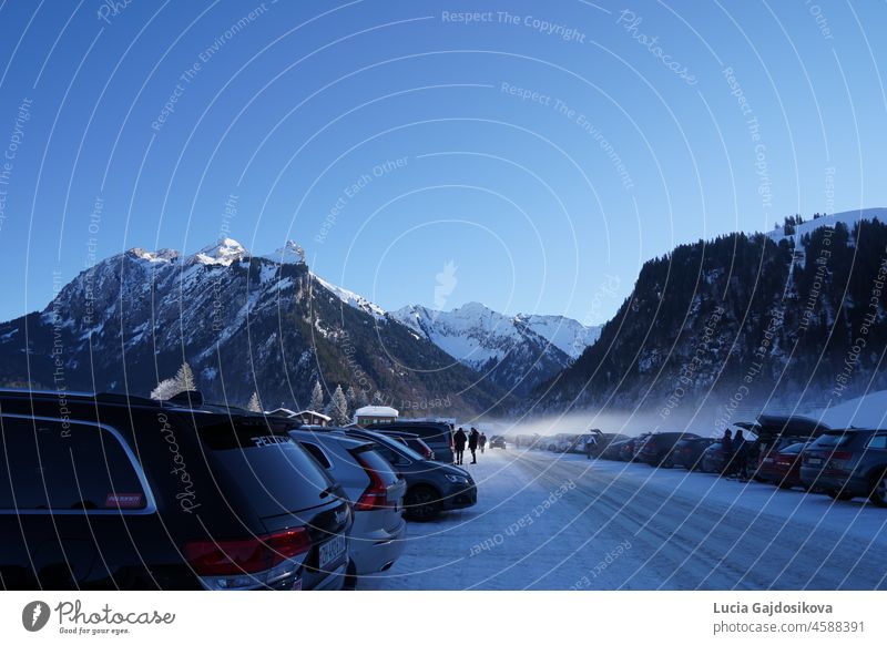 Voller Parkplatz mit Autos im Langlaufgebiet in der Schweiz, umgeben von schneebedeckten Bergen. Die Besucher machen sich bereit, auf die Loipe zu gehen.