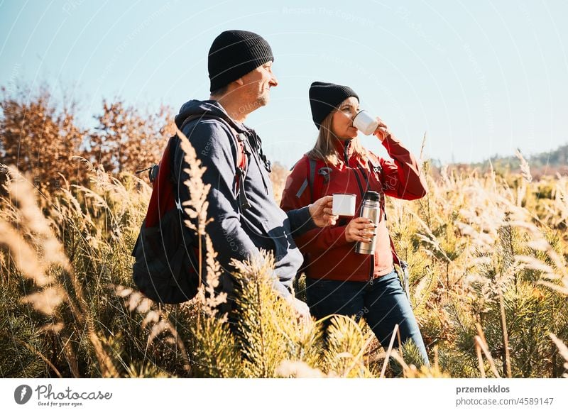 Paar entspannt und genießt den Kaffee während der Urlaubsreise. Menschen stehen auf dem Weg trinken Kaffee. Freunde mit Rucksäcken Wandern durch hohes Gras entlang Weg in den Bergen