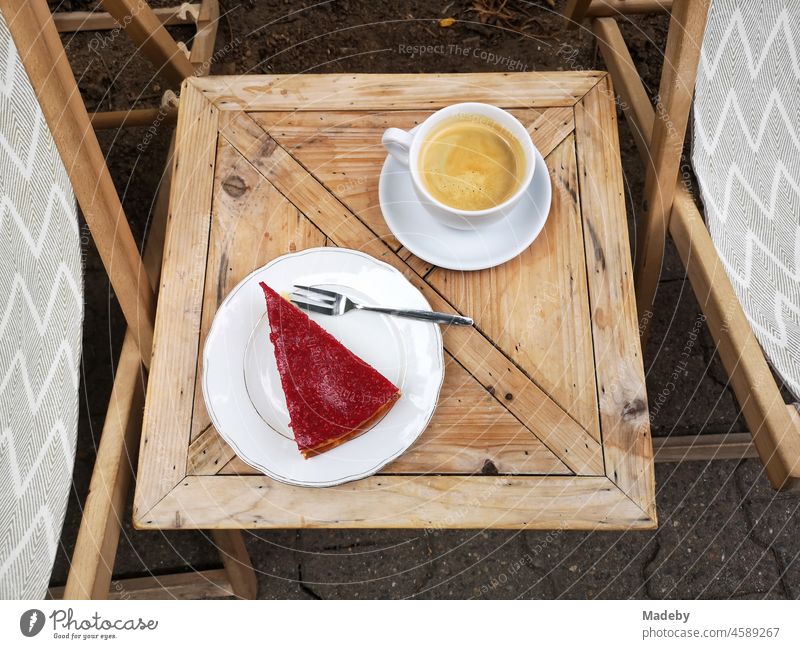 Frischer Kaffee und ein Stück Obstkuchen mit roten Früchten auf einem kleinen Holztisch vor einem Café im Sommer im Nordend von Frankfurt man Main in Hessen