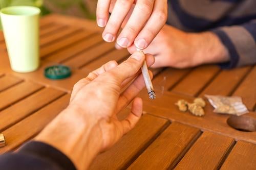 Unbekannte Person, die ihrem Freund auf einer Party einen Marihuana-Joint reicht. Cannabis Gelenk Unkraut teilen Pass Zusammensein kennenlernen Zigarette