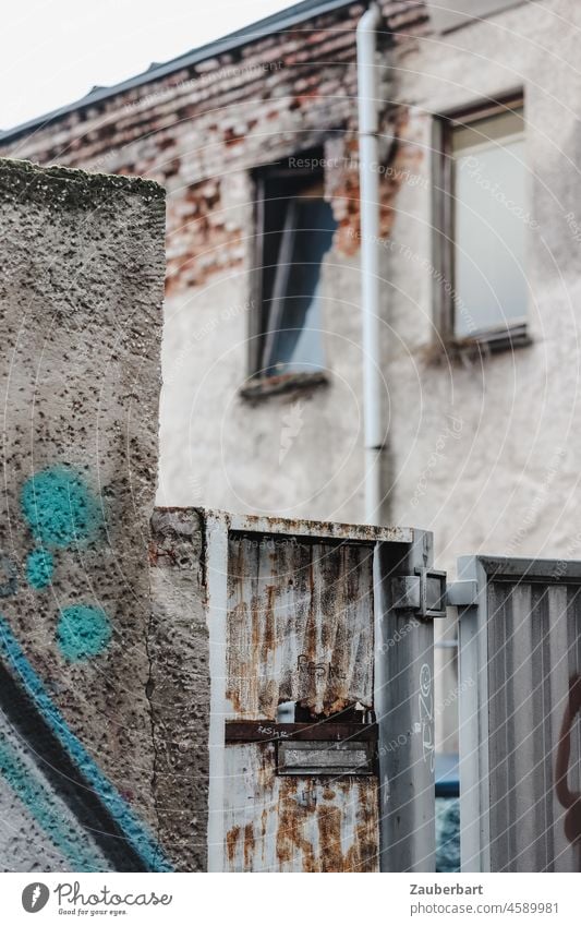 Blick über Mauer, Tor und rostigen Briefkasten auf Hauswand mit zwei Fenstern und Regenrinne Farbe Rost Fassade schäbig Wand Stadt urban Hinterhof trist