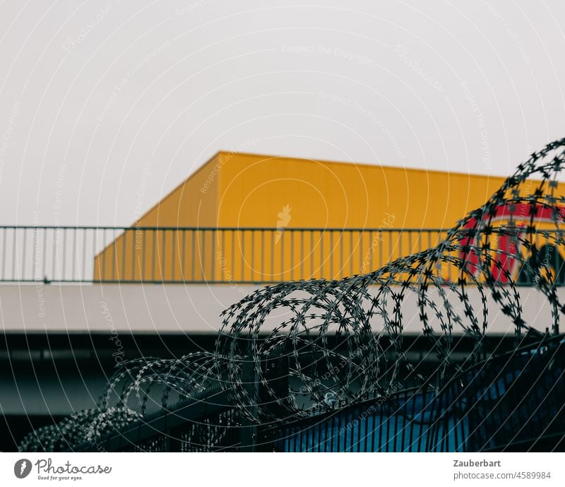 Stacheldraht vor Brücke und quaderförmigem gelbem Lagerhaus Gelände Quader Nato-Draht Grenze Barriere Zaun Sicherheit Schutz bedrohlich gefährlich