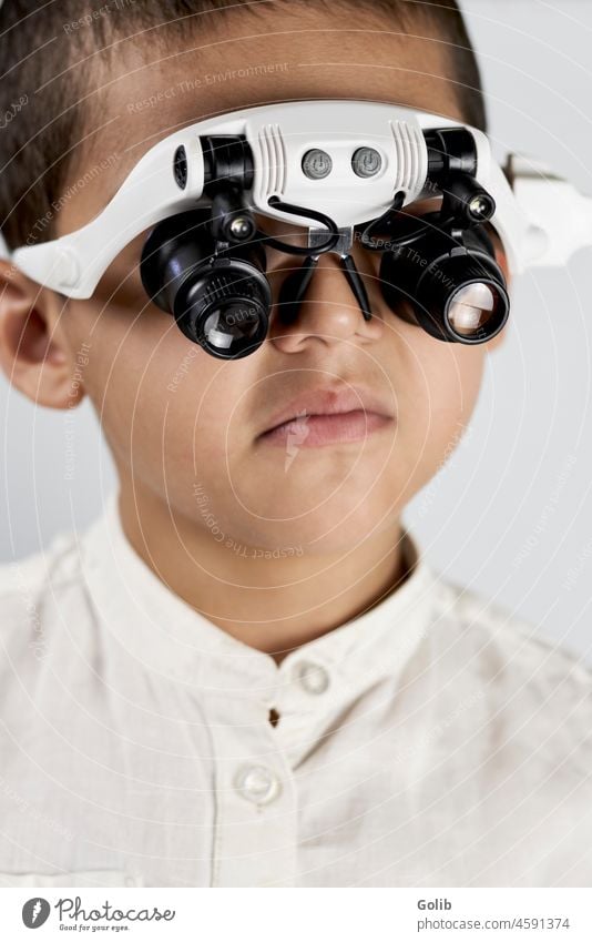 Ein Schuljunge mit Spezialbrille wenig Wissenschaftler vergrößernd speziell Brille zurück zur Schule in die Kamera schauen Nahaufnahme gutaussehend Kind Headset