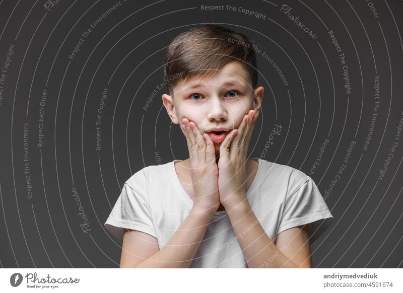 überrascht Junge hält seinen Kopf auf Gesicht isoliert auf grauem Hintergrund mit Platz für Text, Kind unter Schock, Zahnschmerzen. Teenager in weißem T-Shirt