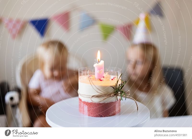 Geburtstagsfeier zu Hause. Glückliche kleine kaukasische Mädchen und niedlichen Baby feiern ersten Geburtstag zu Hause. Candid Lifestyle-Porträt von Kid Blasen Kerzen auf Kuchen. Wohnzimmer mit Fahnen geschmückt.