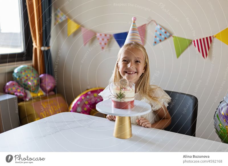 Geburtstagsfeier zu Hause. Glückliche kleine kaukasische Mädchen feiern acht Jahre alt Geburtstag zu Hause. Candid Lifestyle-Porträt von Kid Blasen Kerzen auf Kuchen. Wohnzimmer mit Fahnen geschmückt.