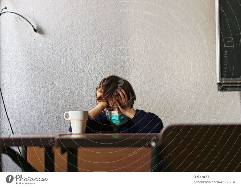 Verzweifeltes Kind am Lehrerpult mit Kaffeetasse, Maske und Hände am Kopf Schule Klassenraum Lehreralltag Pult Verzweiflung lernen corona coronavirus