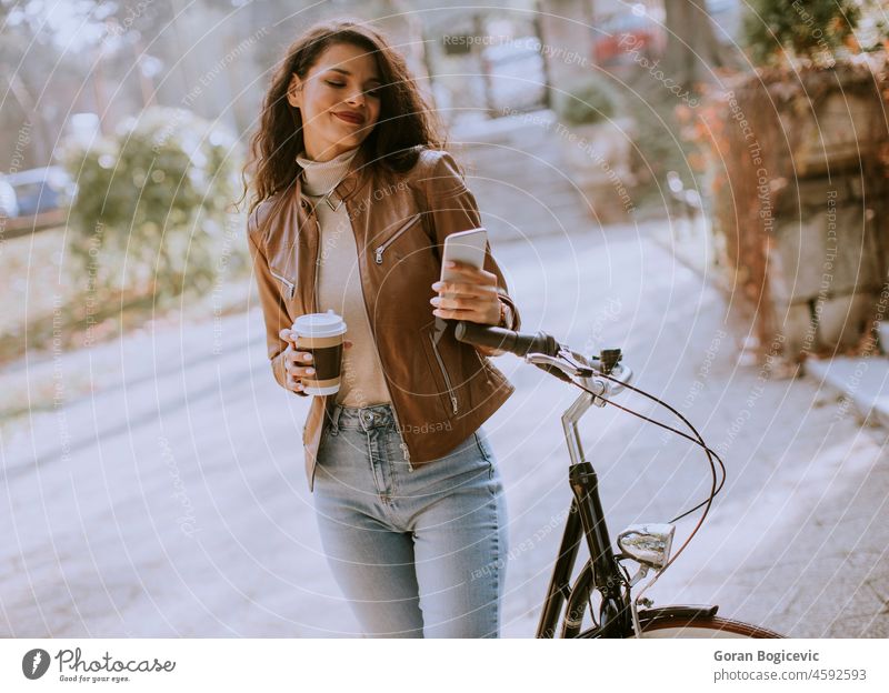 Junge Frau mit Handy trinken Kaffee zu gehen durch das Fahrrad auf Herbsttag Erwachsener attraktiv schön Biker Business lässig Kaukasier Funktelefon Großstadt