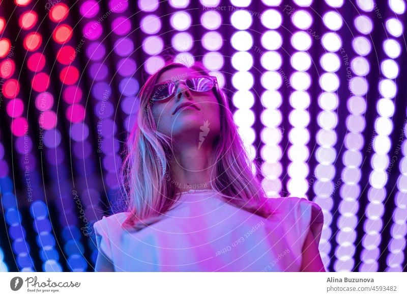 Teenager-Hipster-Mädchen in stilvolle Brille stehen auf lila Tunnel mit Neonlicht Wand Hintergrund, weibliche Teenager-Mode-Modell hübsche junge Frau Blick auf Nachtclub Stadt Licht glühen