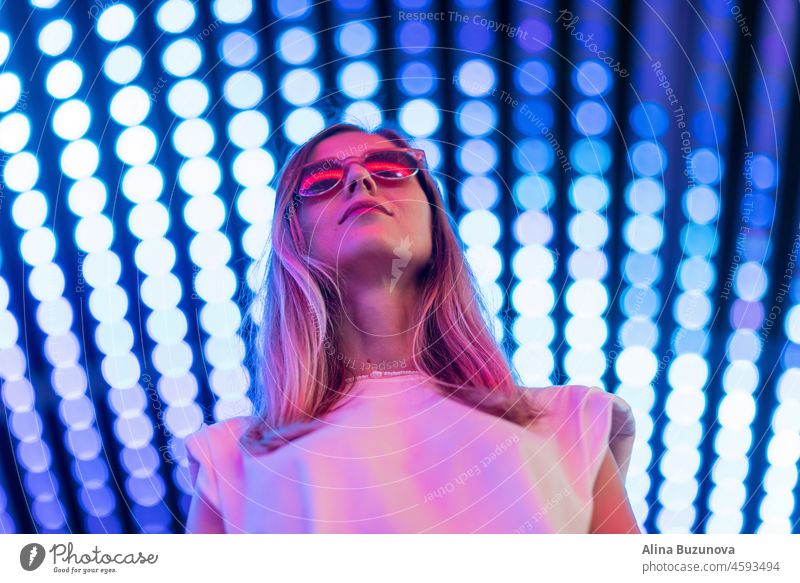 Teenager-Hipster-Mädchen in stilvollen Brillen stehen auf blauen Tunnel mit Neonlicht Wand Hintergrund, weibliche Teenager Mode-Modell hübsche junge Frau Blick auf Nachtclub Stadt Licht glühen
