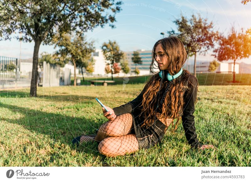 junges Mädchen sitzt auf dem Rasen in einem Park und schaut mit Kopfhörern auf das Smartphone hübsch Sitzen Gras Blick Handy Mobile Telefon sorgenfrei entspannt