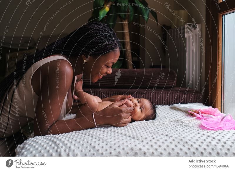 Schwarze Mutter zieht kleines Baby in Windeln an angezogen Body neugeboren Pflege Säuglingsalter Mutterschaft mütterlich Liebe Frau Kind wenig Eltern Sofa Lügen
