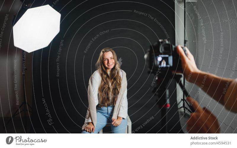 Anonymer Mann fotografiert eine Frau, die auf einem Stuhl in einem professionellen Studio sitzt Fotoapparat Fotograf fotografieren Atelier Gerät trendy Model