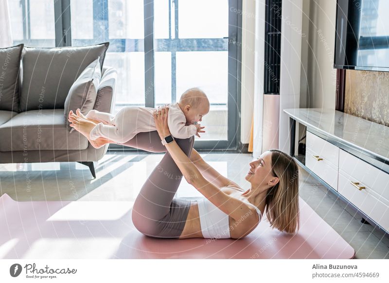 Junge Mutter in Sportkleidung trainiert zu Hause mit ihrem Baby. Online-Schulung während der Quarantäne wegen des Coronavirus Covid-19. Fit und sicher bleiben während der Pandemie-Sperrung. Sport, Fitness, gesundes Konzept