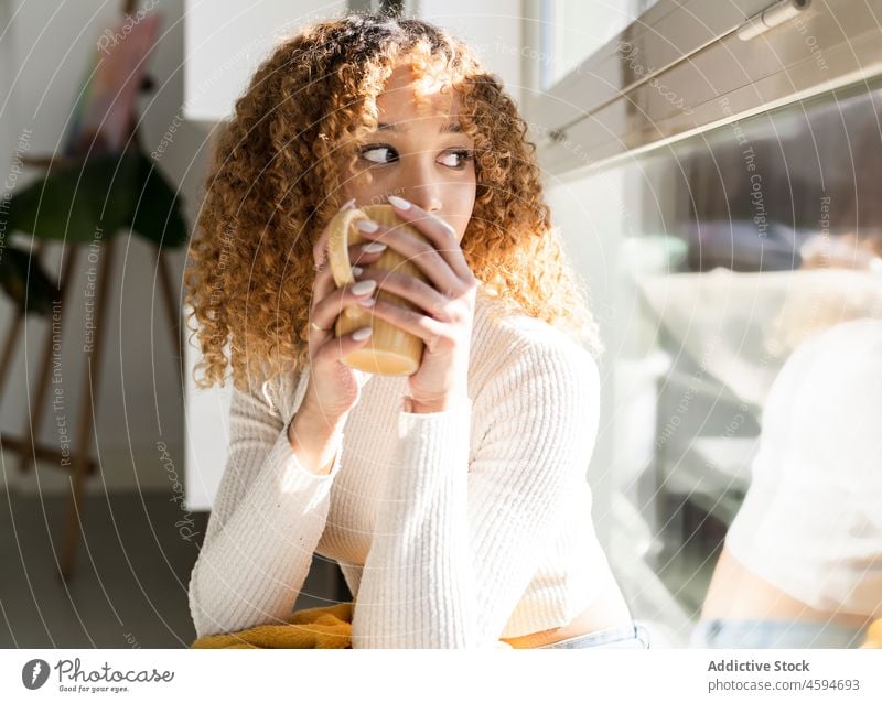 Schwarze Frau sitzt mit Tasse und Decke auf der Fensterbank trinken Fenstersims Getränk gemütlich Komfort Plaid ruhen sich[Akk] entspannen Tee Becher