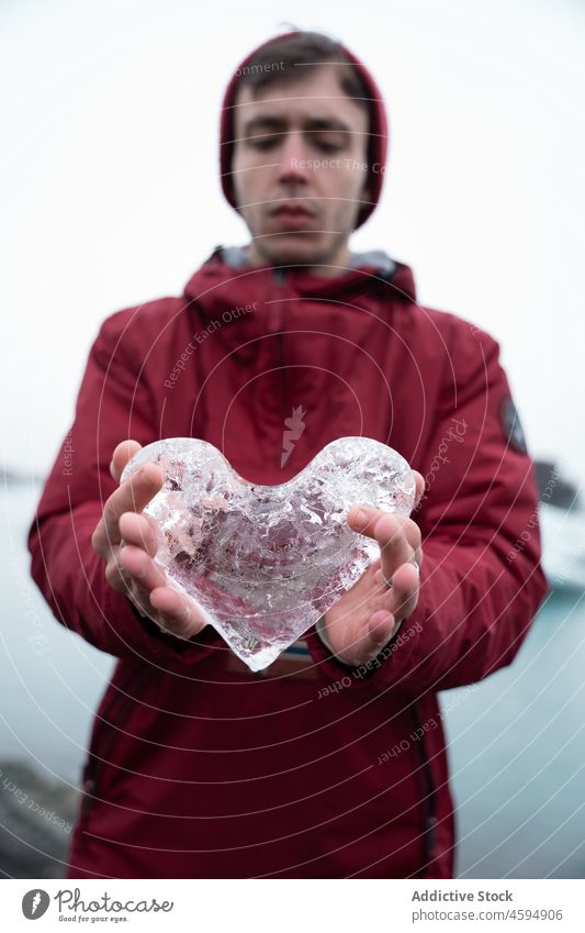 Mann in Oberbekleidung zeigt herzförmiges Eis Reisender kalt Herz gefroren zeigen Symbol Norden Spielfigur männlich Winter manifestieren Frost Klima Tourismus