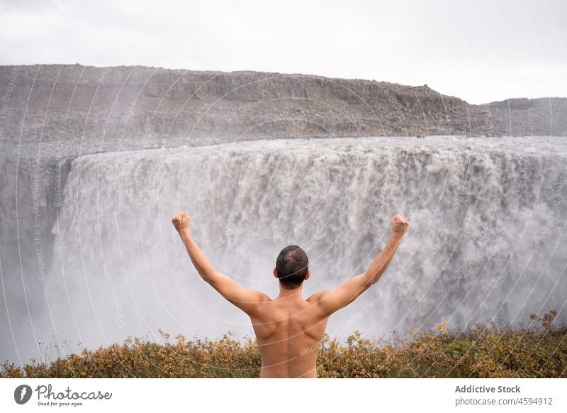 Mann ohne Hemd genießt die Freiheit am Wasserfall Reisender Erfolg feiern erreichen Abenteuer mit der Faust nach oben Aussichtspunkt männlich bewundern