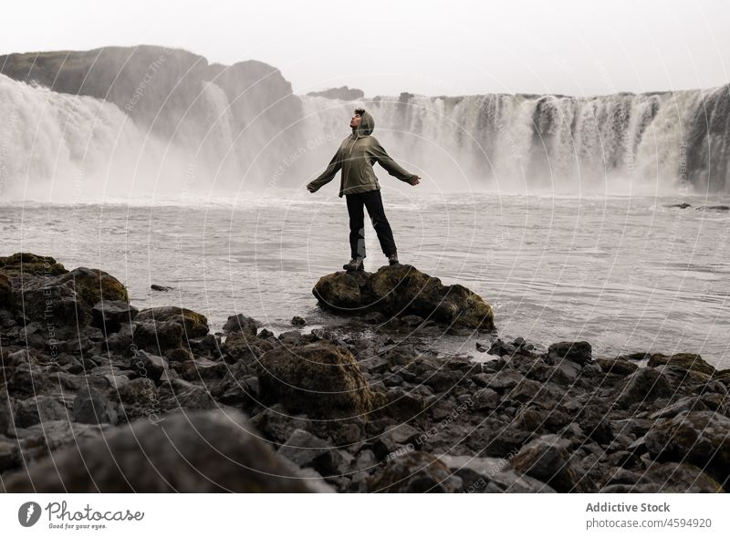 Tourist streckt die Arme aus, während er auf einem Stein in der Nähe eines schäumenden Wasserfalls steht Mann erkunden Freiheit Natur Fernweh Kaskade Harmonie