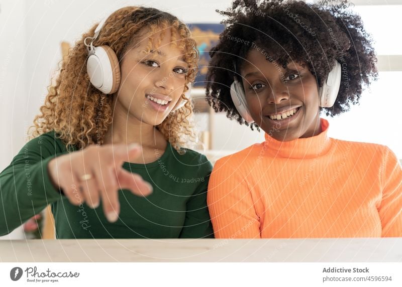 Fröhliche Frauen mit Kopfhörern, die eine Geste des Grußes zeigen Freund positiv vlog gestikulieren Afro-Look soziale Netzwerke Hallo Glück Lächeln Zusammensein