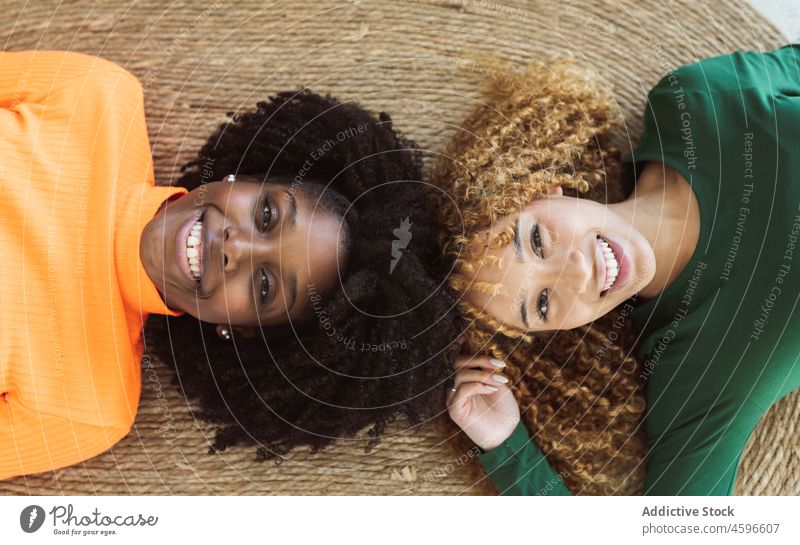 Positive multiethnische Freundinnen, die zusammen auf einem Teppich liegen Frauen Stock Zusammensein Lügen Lächeln Glück Freundschaft sich[Akk] entspannen