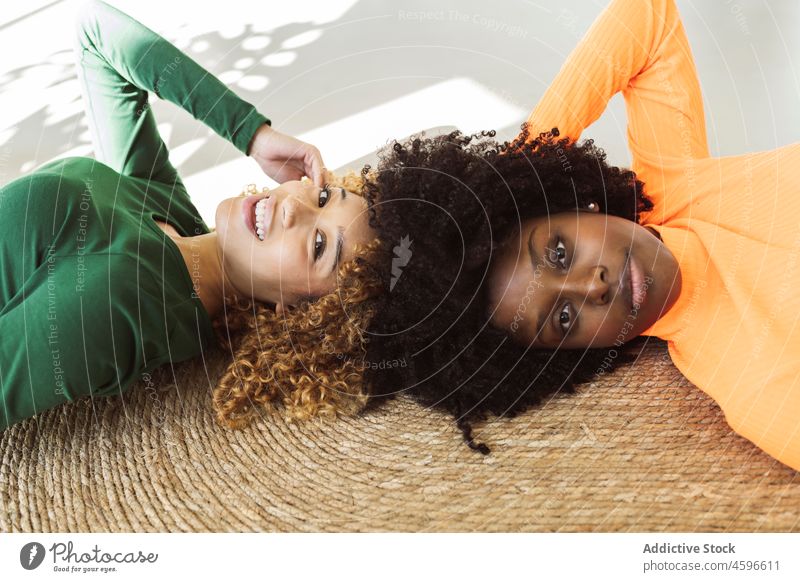 Positive multiethnische Freundinnen, die zusammen auf einem Teppich liegen Frauen Stock Zusammensein Lügen Lächeln Glück Freundschaft sich[Akk] entspannen