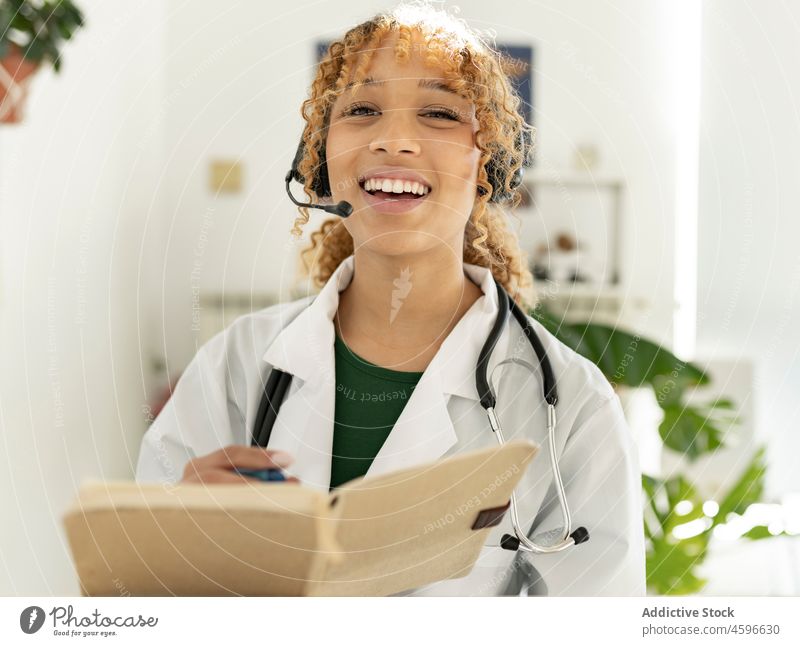 Ärztin mit Headset, Mikrofon, Stethoskop und Notizbuch Frau Arzt Telemedizin medizinisch Lächeln Betreiber Telearbeit konsultieren Videoanruf Arbeit vorbereiten