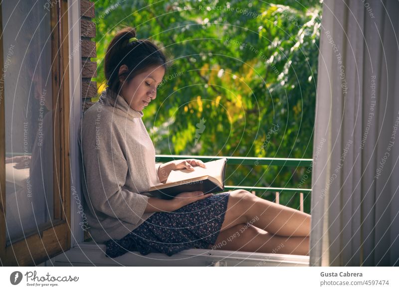 Ein Mädchen liest ein Buch im Rahmen ihres Fensters. lesen Leser Fensterrahmen Bildung Literatur lernen Farbfoto Roman