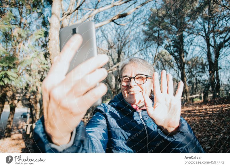 Glückliche reife Frau mit einem Video-Chat durch Smartphone während eines Tages im Wald während einer Reise zu trecken. Kopieren Raum sitzen auf einer Holzbank. Aktive ältere Frau gesunden Lebensstil. Rufen Enkelkinder