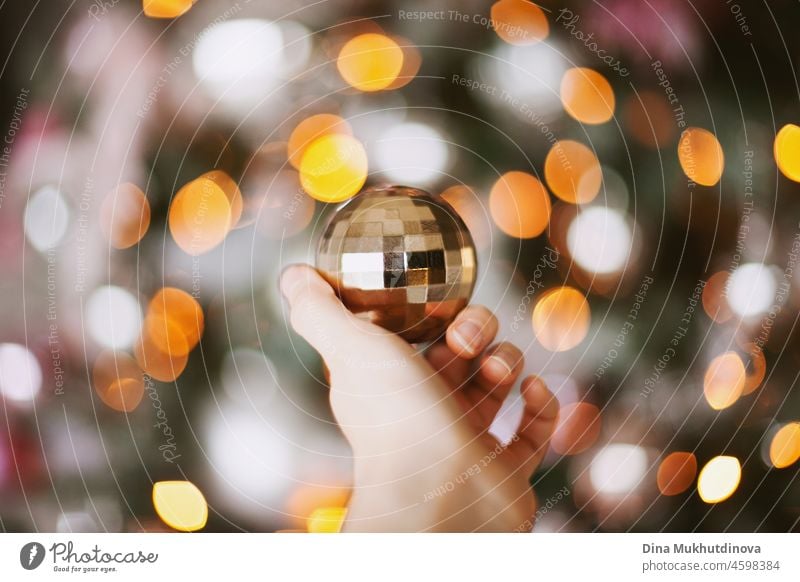 Hand hält eine glänzende goldene Weihnachtsschmuck mit Weihnachtsbaum Lichter Bokeh als Hintergrund Glanz Kugel festlich fröhlich Ornament Jahr Feier