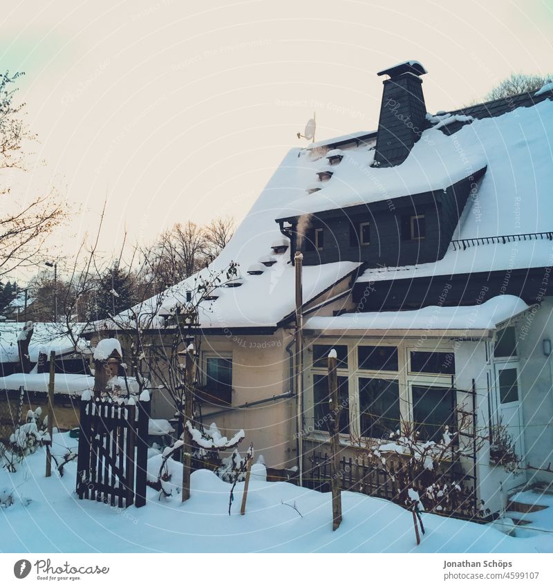 Einfamilienhaus im Winter mit Schnee und Schornstein Rauch heizen Heizkosten Heizung Idylle Winterstimmung kalt Heizkostenanstieg Energie Wärme Haus Dach