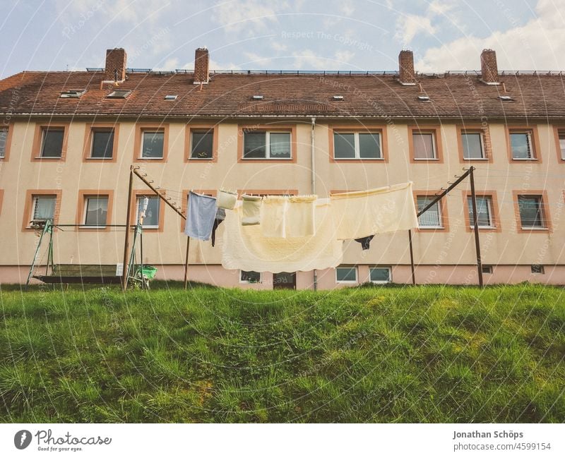 Wäscheleine auf der Wiese vor Mehrfamilien Wohnhaus Mehrfamilienhaus Wohnblock Haus wohnen Alltag wäsche aufhängen Wäsche waschen Hof trocknen Alt Deutschland