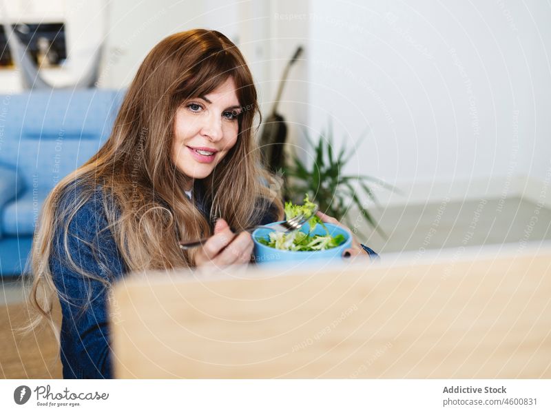 Zufriedene Frau isst, während sie auf dem Laptop surft essen Lebensmittel Mahlzeit Mittagessen online Wohnzimmer Freizeit Zeitvertreib Video feminin heimisch