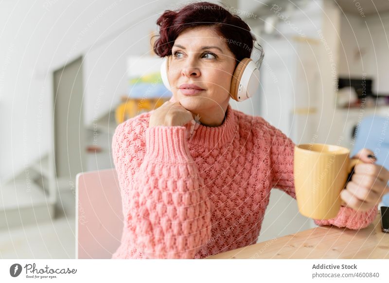 Frau mit Tablette, die ein Getränk trinkt und über Kopfhörer Musik hört trinken Heißgetränk Tasse Erfrischung nachdenklich modern Gerät Apparatur benutzend