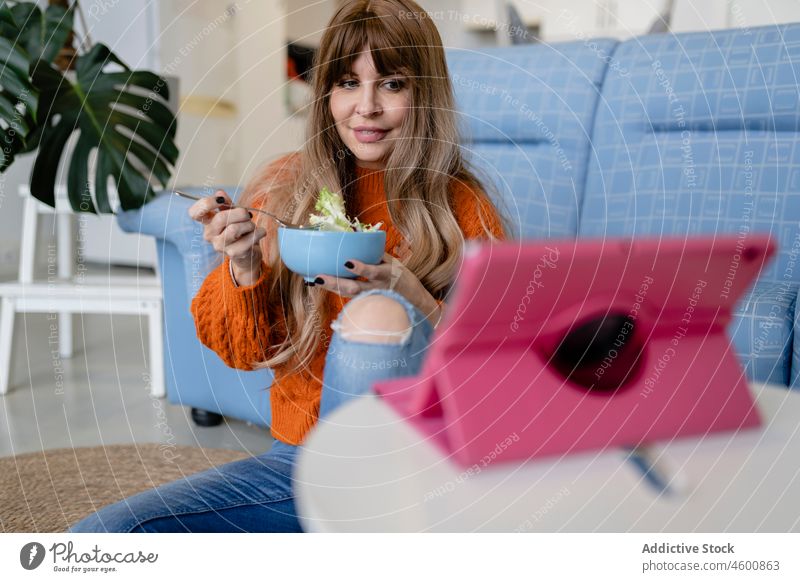 Frau isst, während sie ein Video ansieht essen Tablette Lebensmittel Mahlzeit online Wohnzimmer Freizeit Zeitvertreib feminin heimisch Appartement Dame lässig