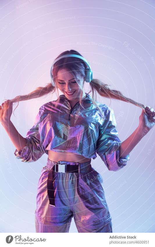 Futuristische Frau in stilvollem Outfit steht im Studio mit Neonbeleuchtung neonfarbig leuchten Lächeln zuhören Stil futuristisch Kopfhörer 80s Persönlichkeit