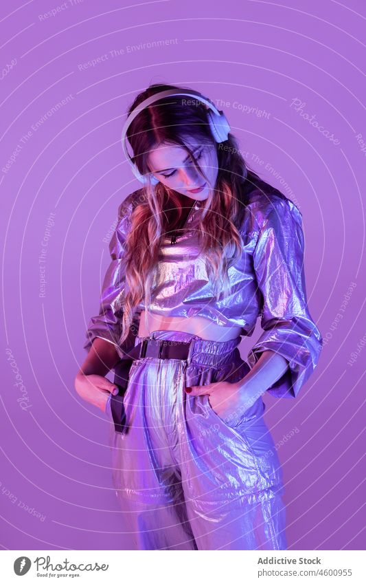 Futuristische Frau in stilvollem Outfit steht im Studio mit Neonbeleuchtung neonfarbig leuchten zuhören Stil futuristisch nachdenklich Kopfhörer 80s