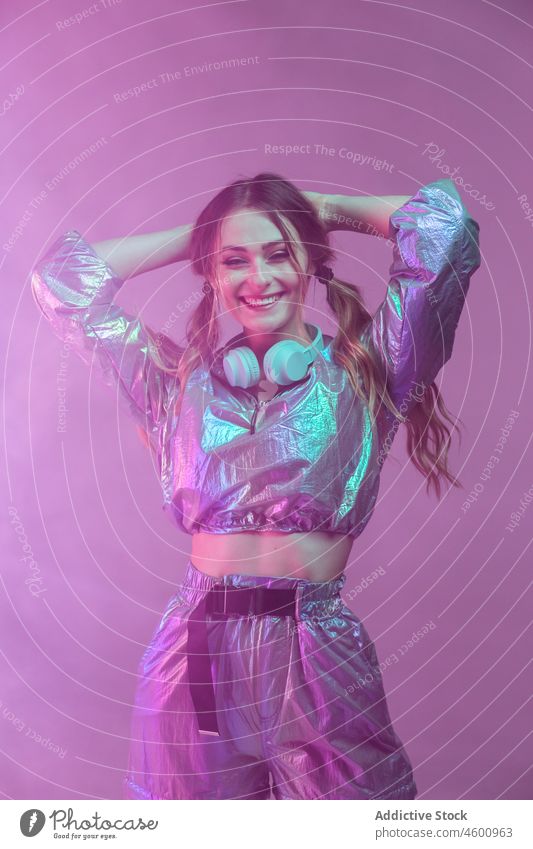 Futuristische Frau in stilvollem Outfit steht im Studio mit Neonbeleuchtung neonfarbig leuchten Stil Lächeln futuristisch Kopfhörer 80s Persönlichkeit Glück