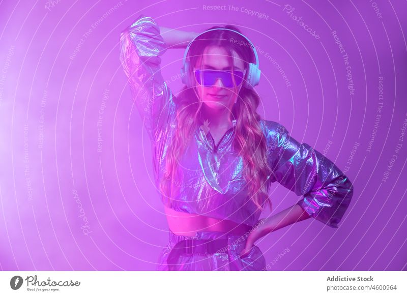 Futuristische Frau in stilvollem Outfit steht im Studio mit Neonbeleuchtung neonfarbig leuchten zuhören Vorschein Stil futuristisch Kopfhörer 80s Persönlichkeit
