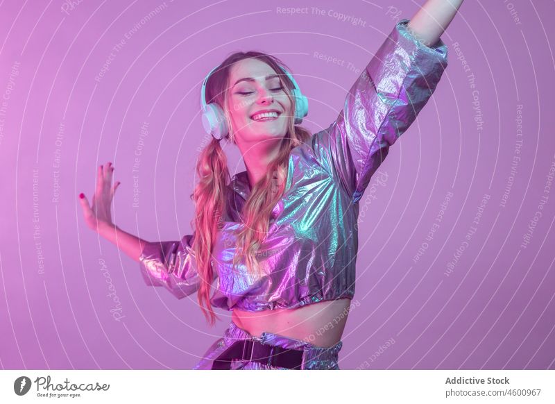 Futuristische glückliche Frau in stilvollem Outfit steht im Studio mit Neonbeleuchtung neonfarbig leuchten zuhören Stil Lächeln Augen geschlossen futuristisch