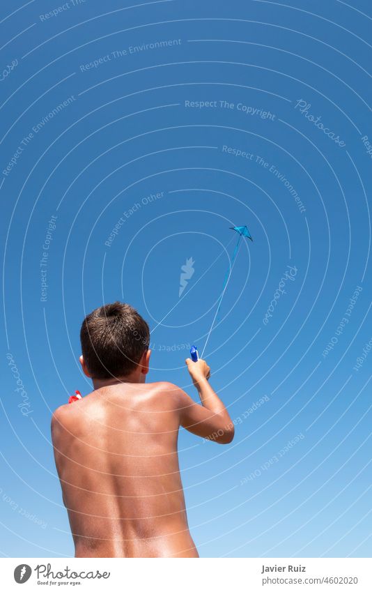 Junge auf dem Rücken, der mit einem Lenkdrachen spielt, von unten gesehen, mit dem Drachen hoch oben im blauen Himmel an einem Sommertag, Kopie des Weltraums