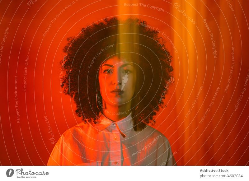 Ernste hispanische Dame in einem Studio mit roten Neonröhren stehend Frau ernst Model Porträt Vorschein Stil selbstbewusst selbstsicher neonfarbig traumhaft
